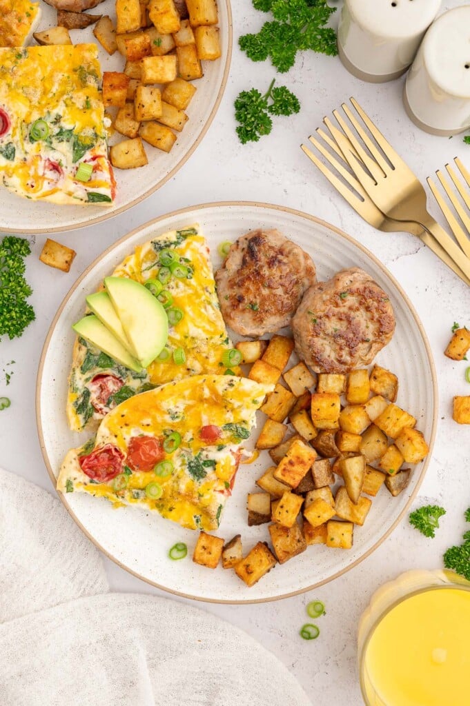 Breakfast potatoes on a white plate with two slices of egg white frittata and chicken sausage on the side and another plate of food on the side.
