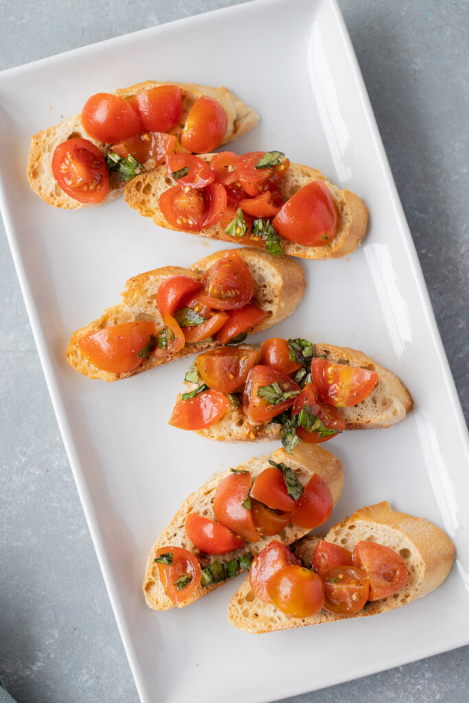 6 Bruschetta baguette toasts on a white platter on a grey background
