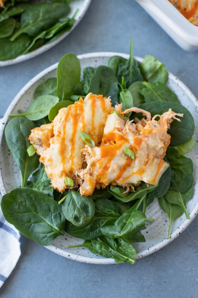Two scoops of buffalo chicken on a bed of spinach on a white plate