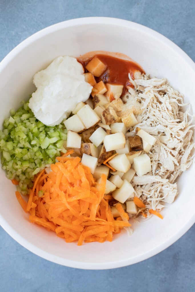 Ingredients for buffalo chicken casserole with buffalo sauce and potatoes in a white bowl all separated