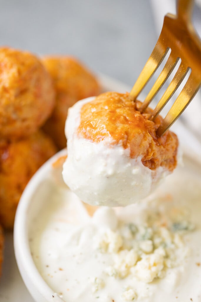 A buffalo chicken meatball on a fork being dipped into a bowl of blue cheese