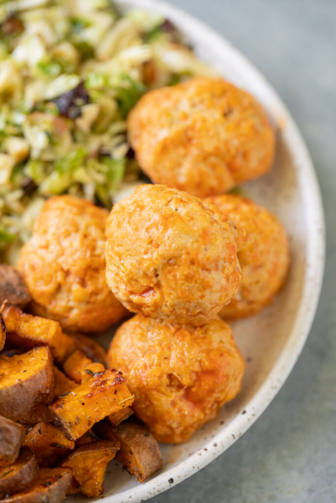 A white plate with buffalo chicken meatballs with potatoes and salad on the side