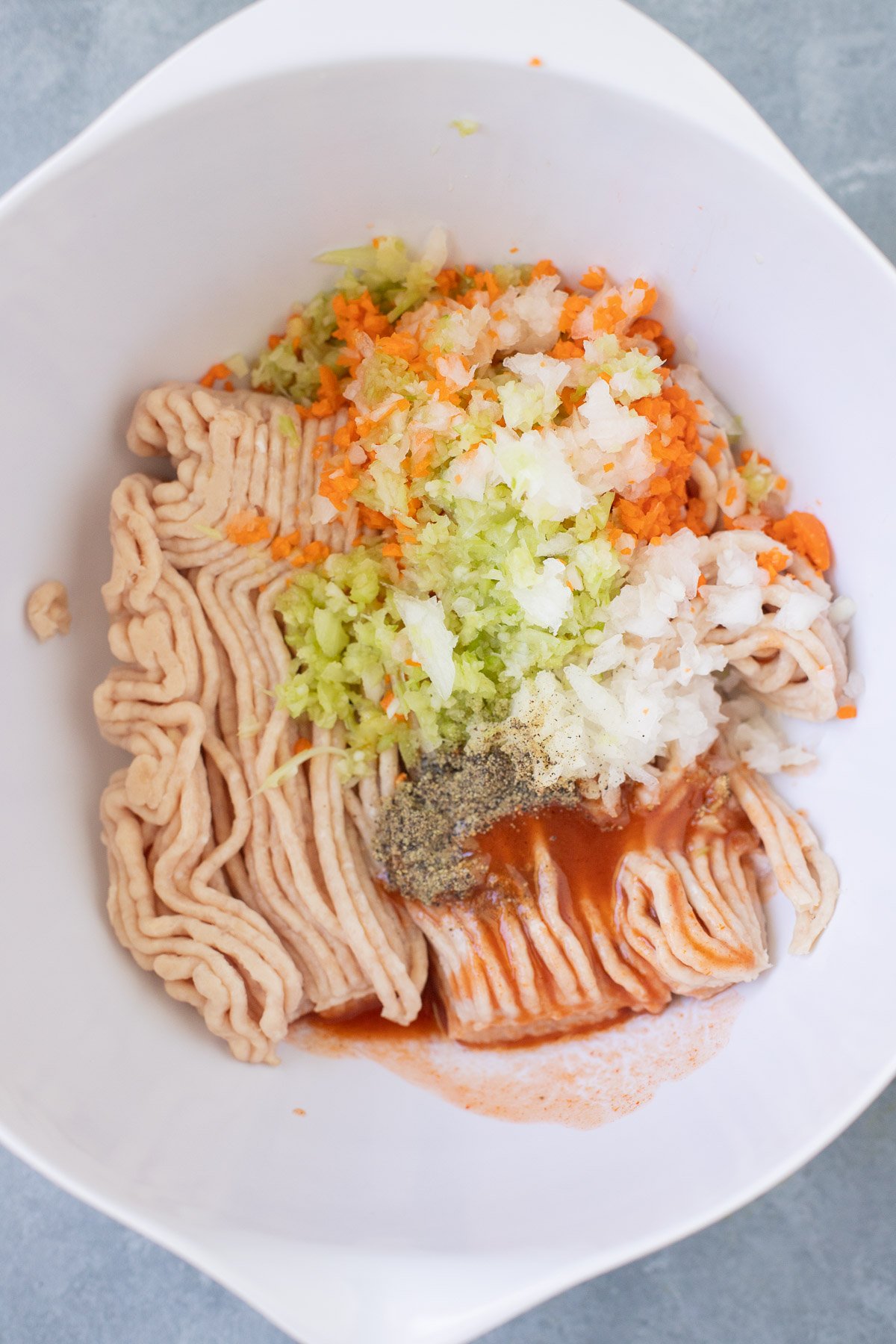 A white bowl with ingredients for buffalo chicken meatballs before being mixed