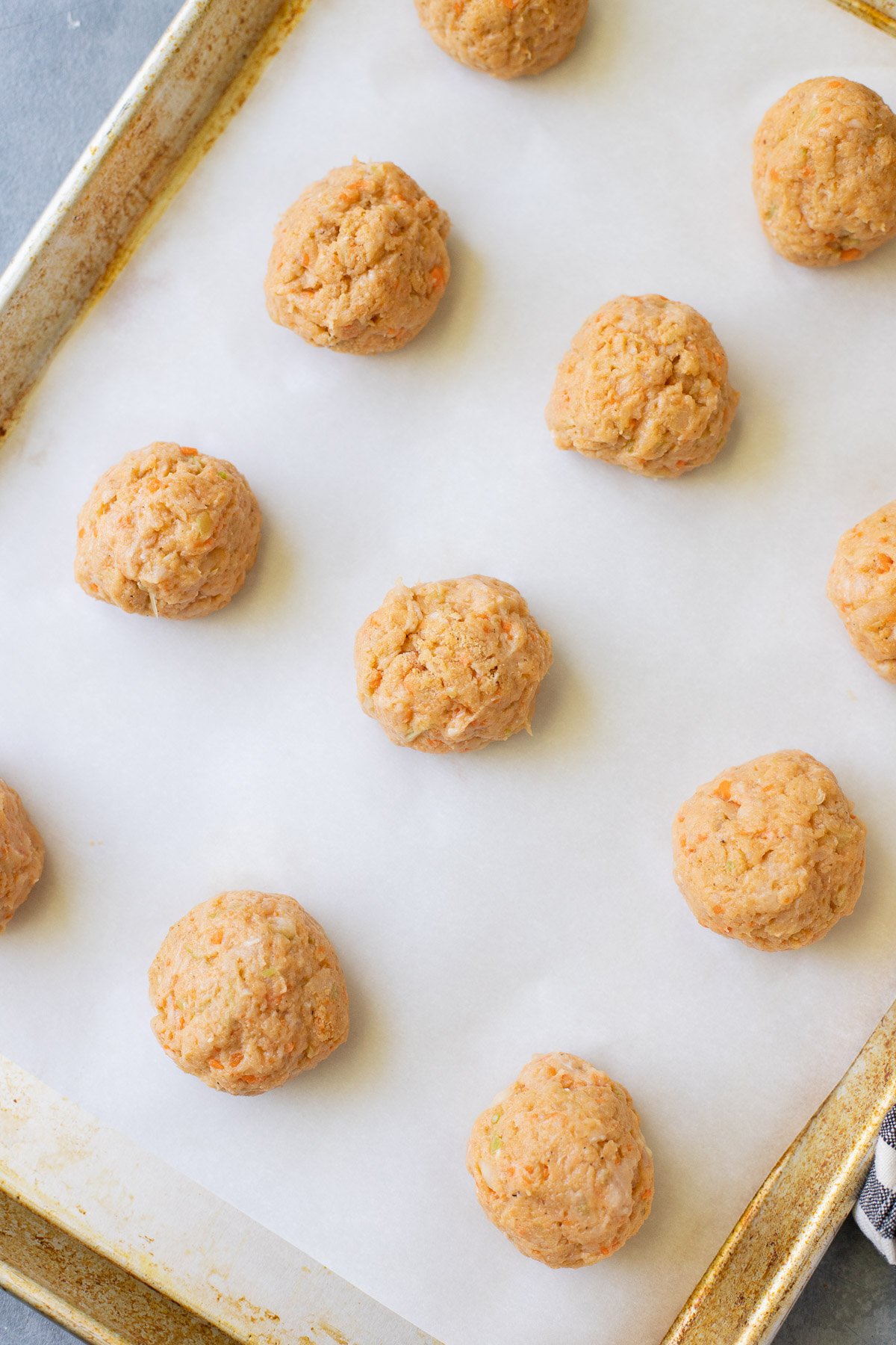 A baking sheet with parchment paper with uncooked buffalo chicken meatballs on it