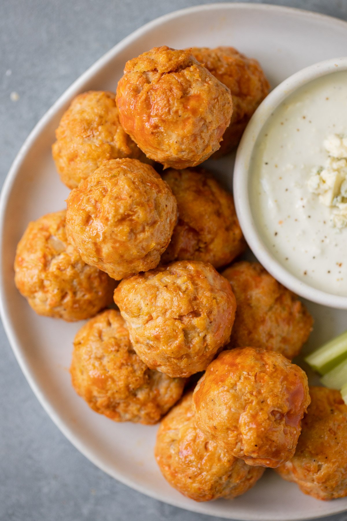 Buffalo Chicken Meatballs stacked on a white plate with blue cheese on the side a grey background