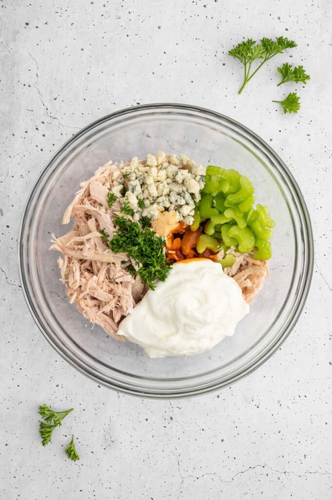 Ingredients for buffalo chicken salad in a clear bowl before being mixed together.