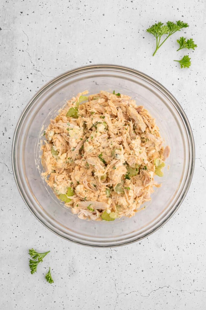 Mixed together buffalo chicken salad in a clear bowl on a grey background