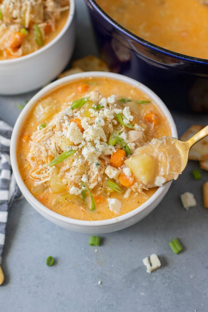 A close up of Buffalo Chicken Soup in a white bowl on a grey background with a spoonful being taken out