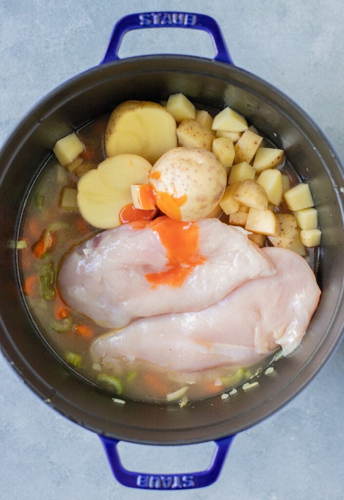 Raw chicken, potatoes, broth and buffalo sauce added to a stock pot with cooked carrots, celery, onion and garlic to make buffalo chicken soup