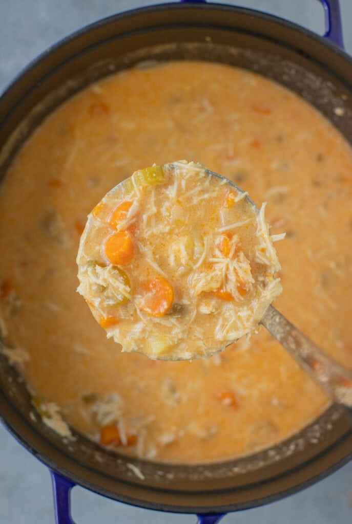 A ladle of buffalo chicken soup being taken out of a stock pot full of buffalo chicken soup