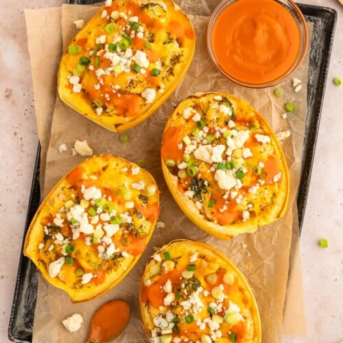 Buffalo Chicken Spaghetti Squash Boats on a parchment lined baking sheet with a bowl of buffalo sauce on the side.