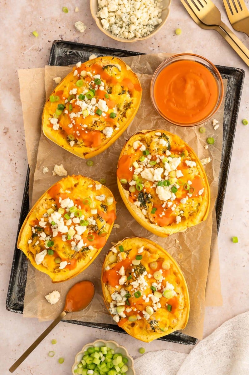 Buffalo Chicken Spaghetti Squash Boats on a parchment lined baking sheet with a bowl of buffalo sauce on the side.