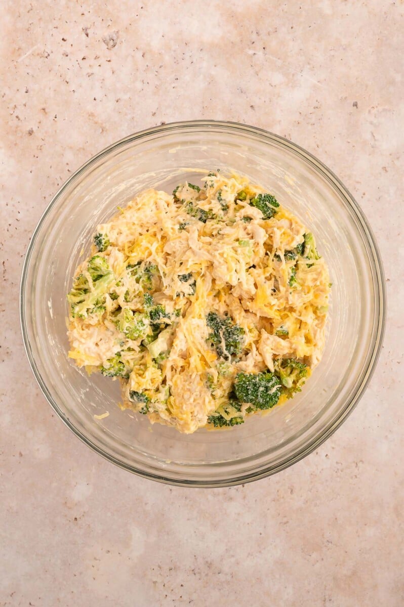 Cooked and shredded chicken, broccoli, hot sauce, yogurt and half the shredded cheese in a bowl. 