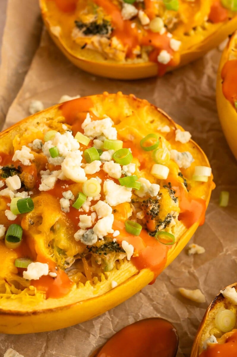 A close up of buffalo chicken spaghetti squash topped with cheese, green onions, and buffalo sauce on a parchment lined baking sheet.