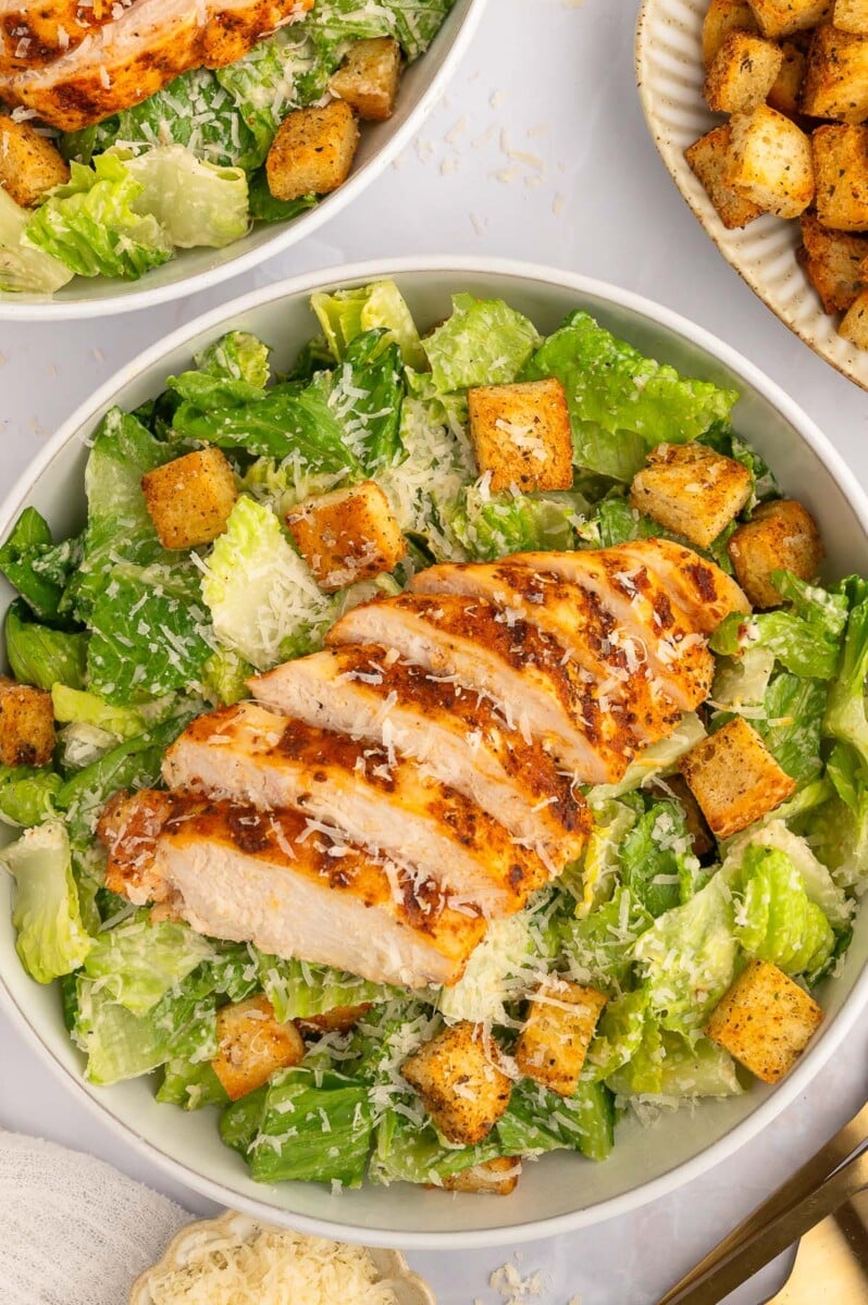 A sliced grilled chicken caesar salad in a white bowl.