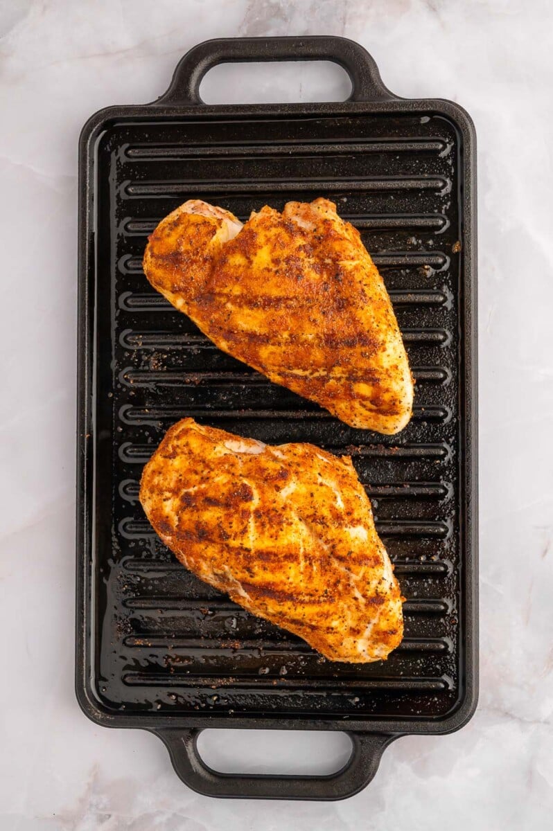 Two grilled chicken breasts on a black stovetop grill.