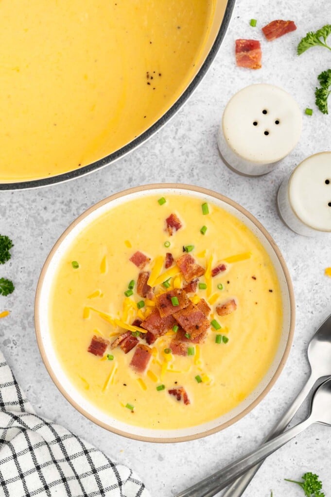 A bowl of cauliflower soup with bacon, cheese and herbs on top with a dutch oven of the soup on the side