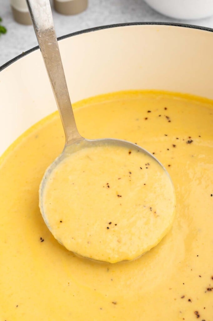 A ladle taking a scoop out of a dutch oven of cheesy cauliflower soup