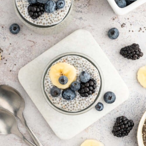 An overhead shot of two jars of chia seed pudding topped with berries and banana slices.