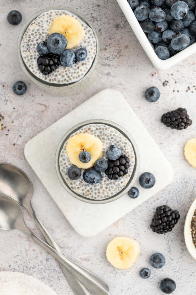 An overhead shot of two jars of chia seed pudding topped with berries and banana slices.