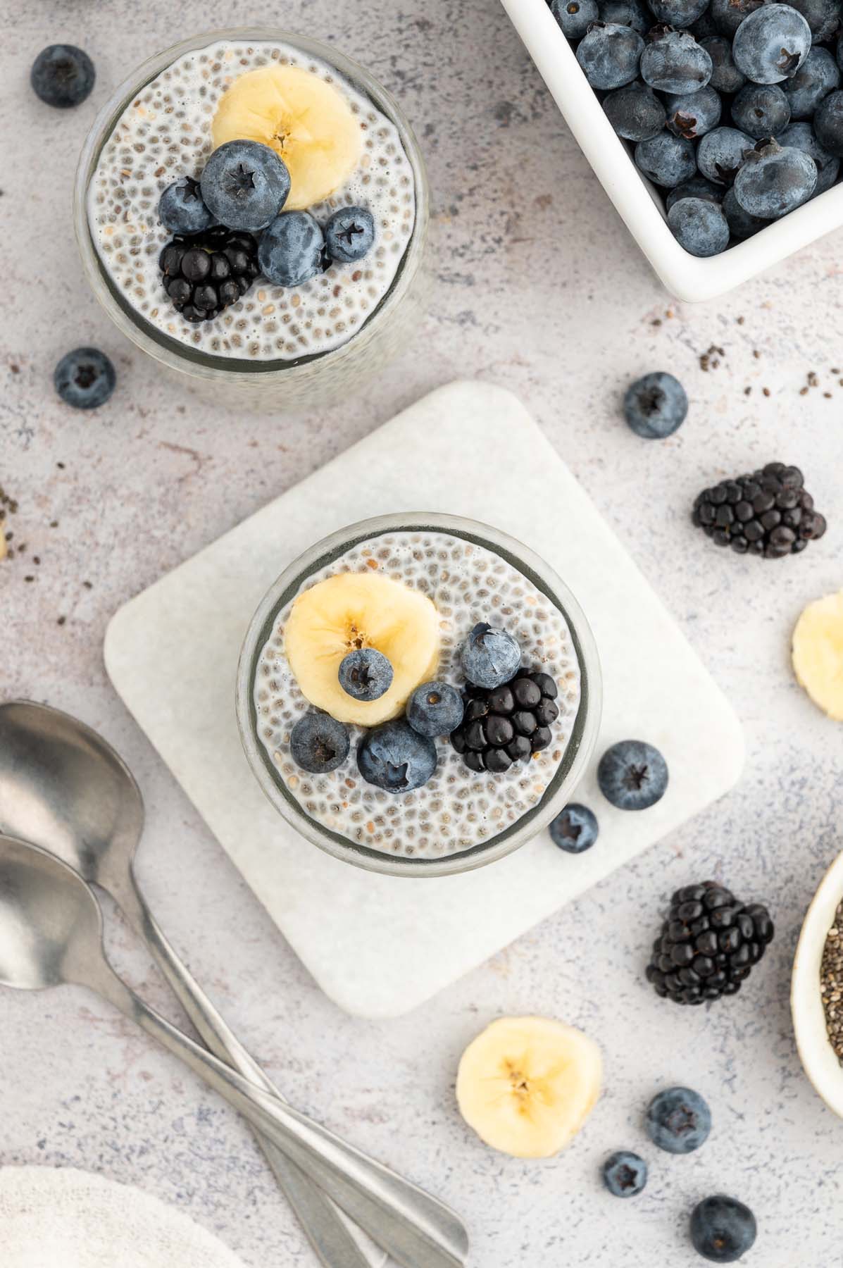 An overhead shot of two jars of chia seed pudding topped with berries and banana slices.