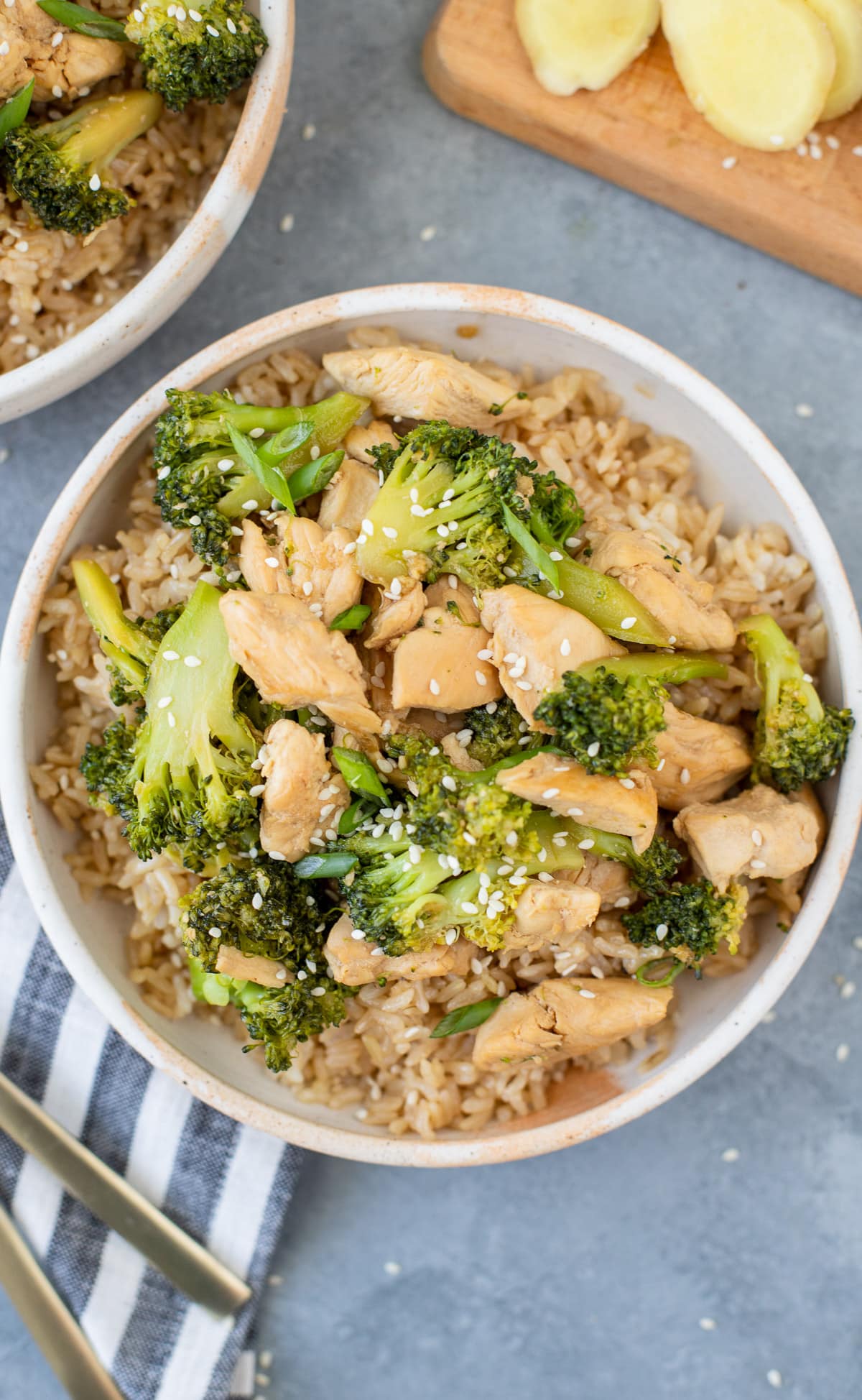 Easy Chicken and Broccoli Stir Fry in a white bowl on a grey background with a bowl and cutting board off to the side