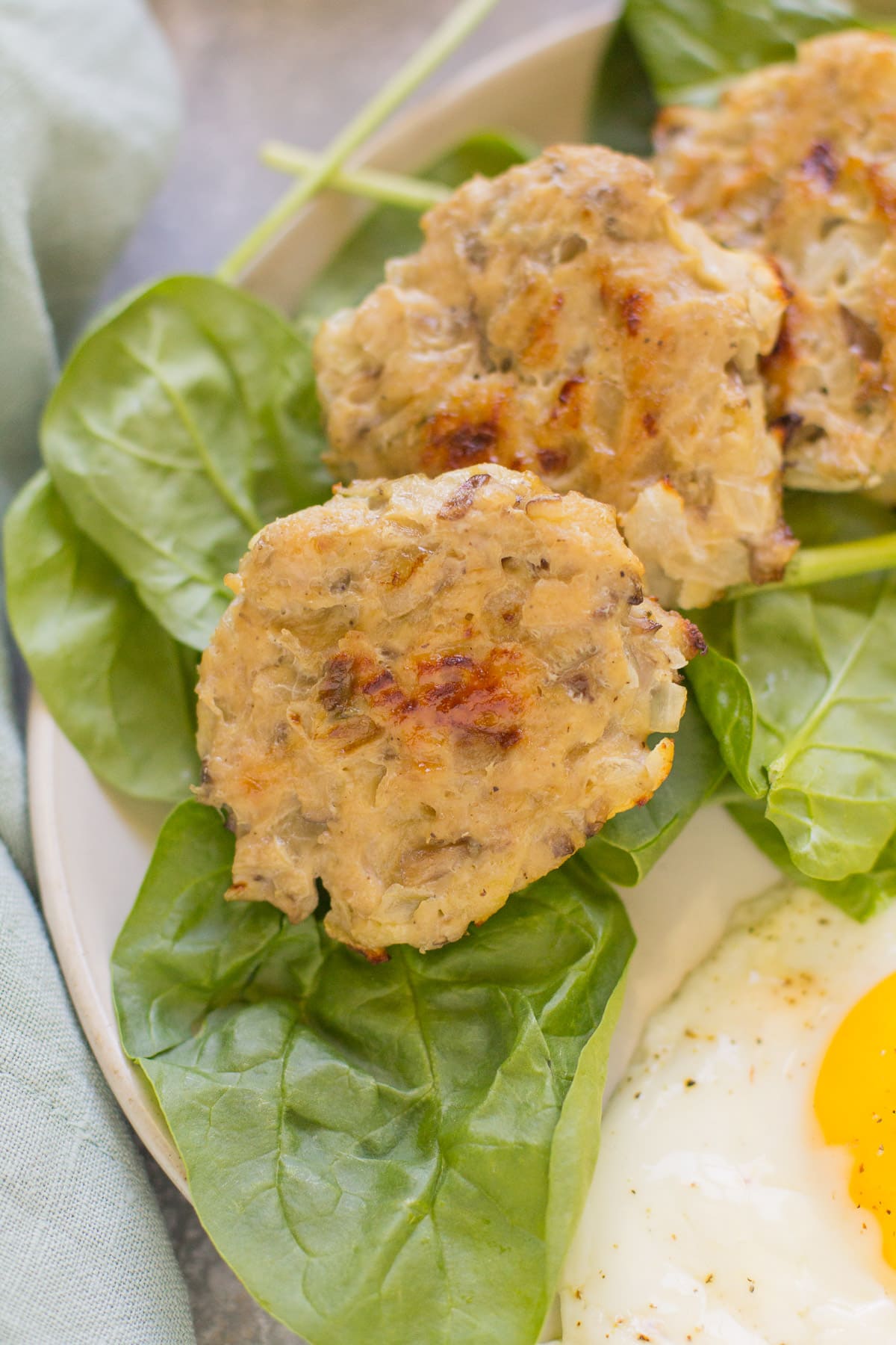 A close up of chicken breakfast sausage on a bed of spinach with eggs on a white plate