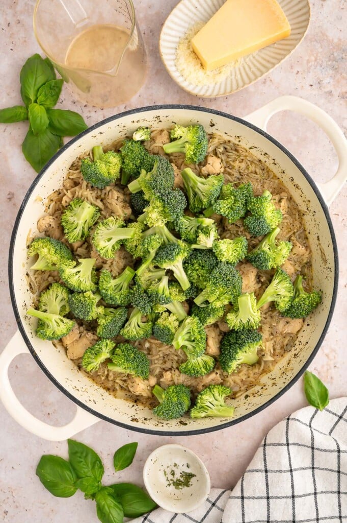 Broccoli added to the top of a one pot chicken dish before stirring in in a dutch oven.