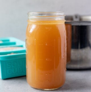 A close up of a container of homemade chicken broth with a pot off to the side