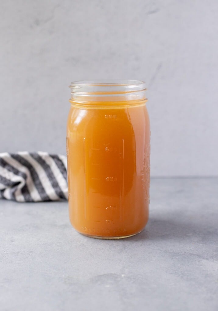 A close up of chicken broth in a glass jar on a grey background