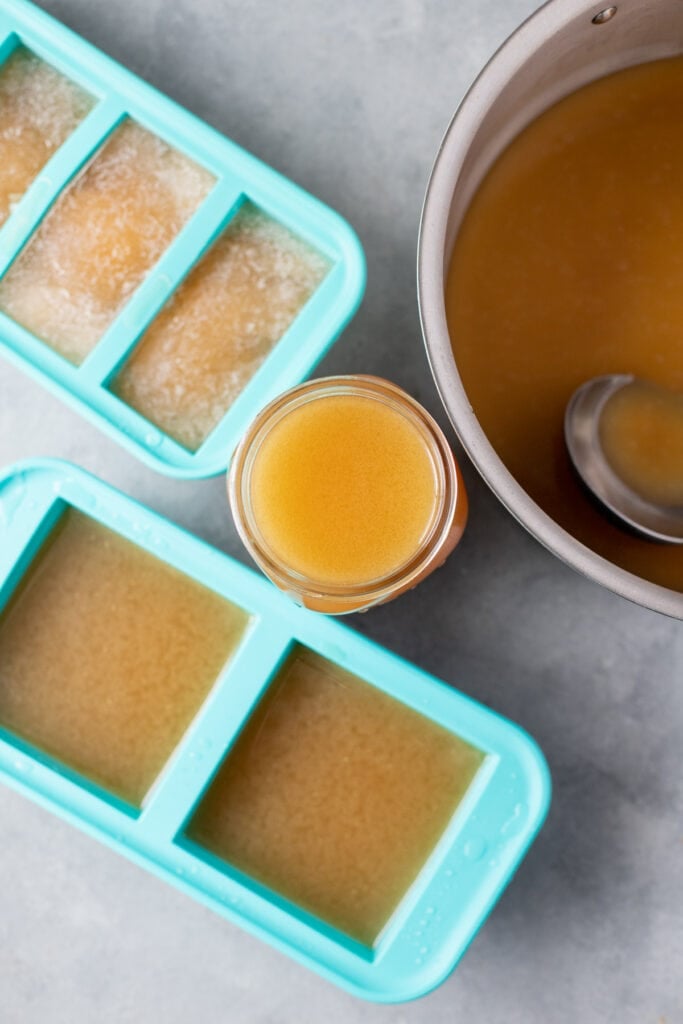 Homemade chicken broth in souper cubes, a glass jar and a pot off to the side