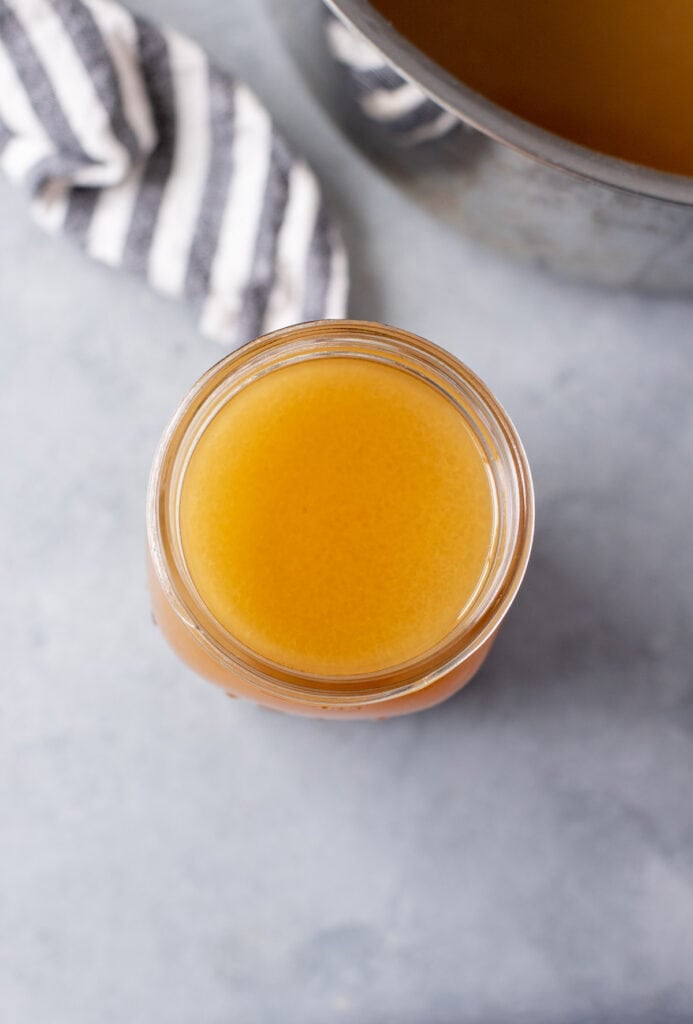 An overhead image of chicken broth on a grey background with a pot off to the side