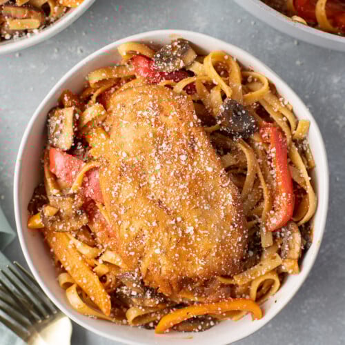 An overhead shot of chicken cacciatore in a bowl with a fork and bowl on the side