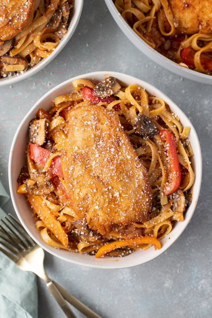 An overhead shot of chicken cacciatore in a bowl with a fork and bowl on the side