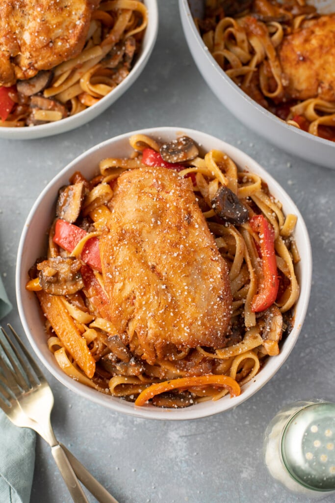 An overhead shot of chicken cacciatore in a bowl with a fork and bowl on the side