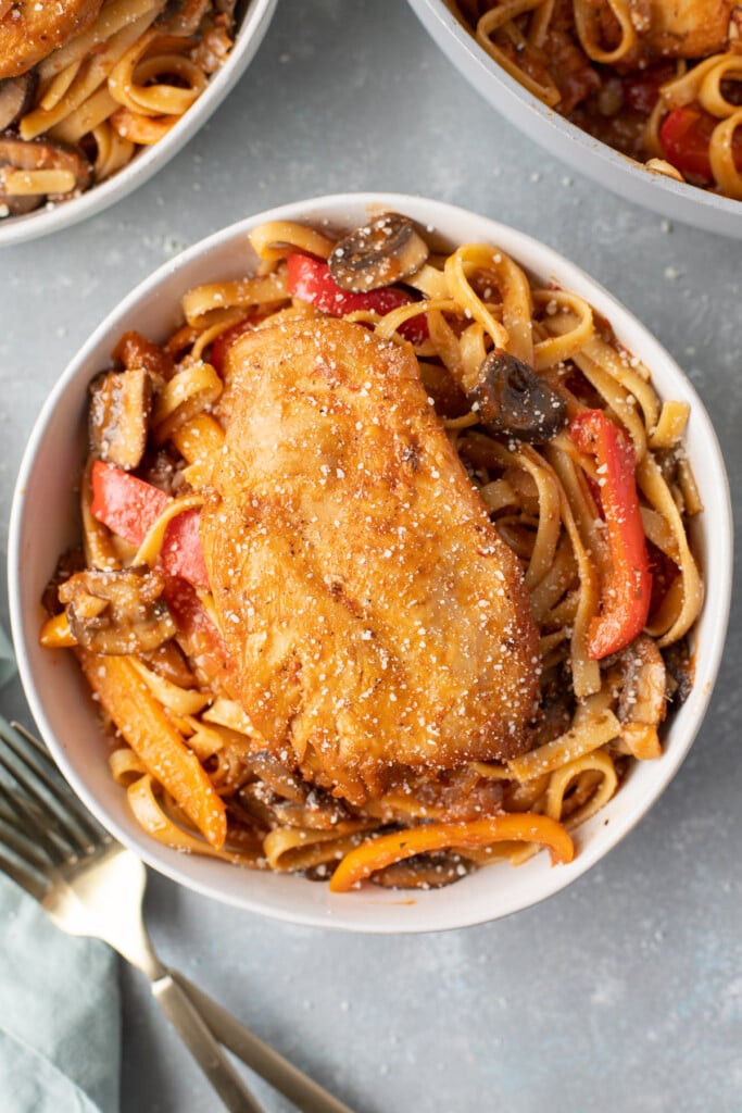 An overhead shot of chicken cacciatore in a bowl with a fork and bowl on the side