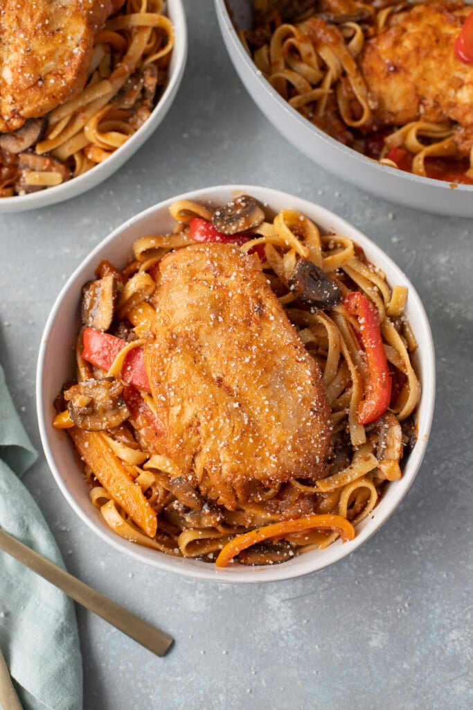 An overhead shot of chicken cacciatore in a bowl with a fork and bowl on the side