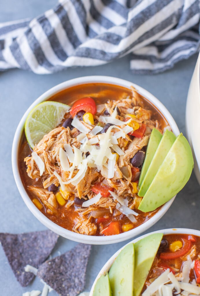 Chicken enchilada soup in a bowl with avocado and limes on it