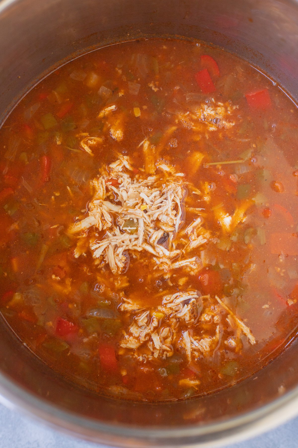 shredded chicken being added back to a pot of chicken enchilada soup