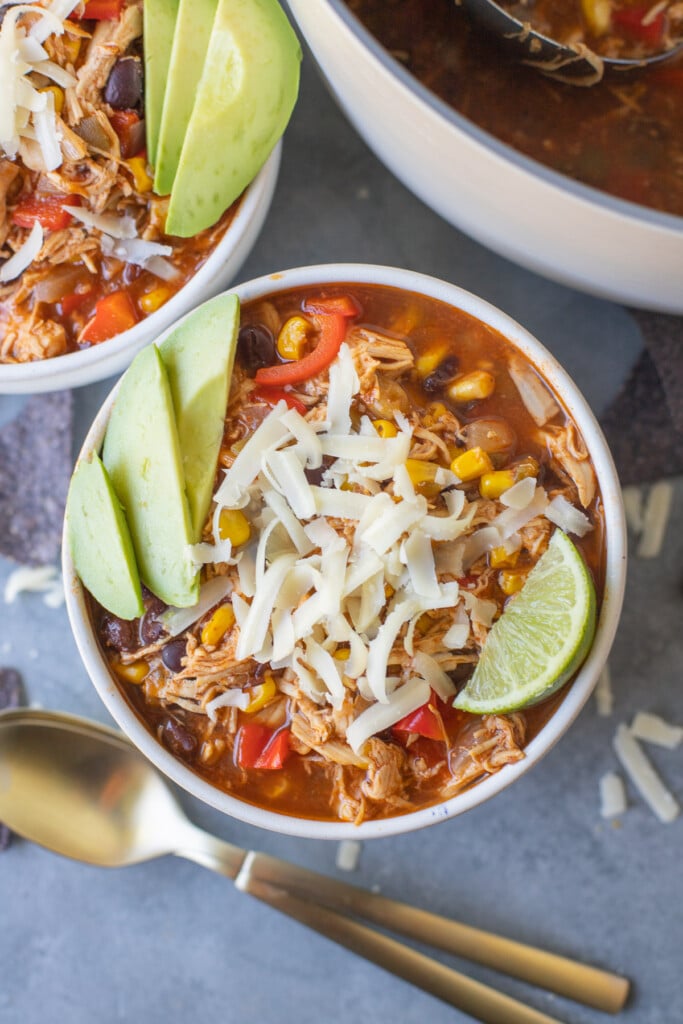 A close up of chicken enchilada soup in a bowl on a grey background