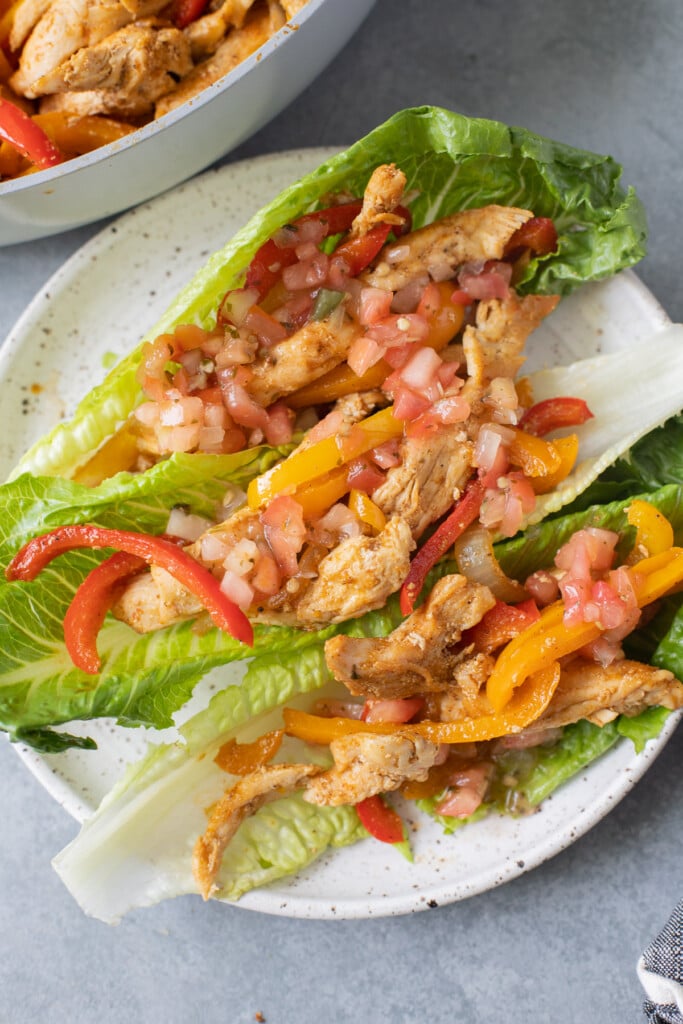Whole30 Chicken Fajitas on a white plate with a grey background and a pan of fajitas in the background