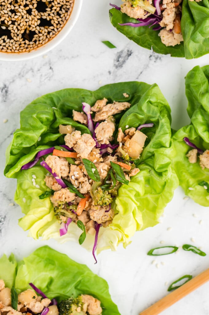 An overhead shot of a chicken lettuce wrap on a marble background with more on the side