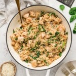 An overhead shot of chicken orzo in a dutch oven with parsley and parmesan on the side in small bowls