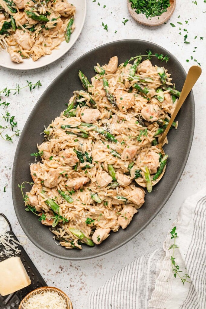 An overhead shot of a grey platter of chicken orzo on a marble background with another plate of chicken orzo on the side