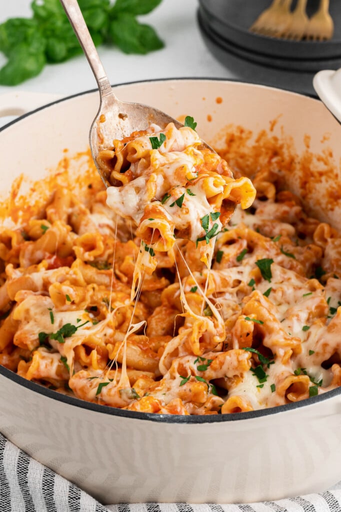 A white dutch oven with chicken parmesan pasta with a spoon taking a large spoonful out of it
