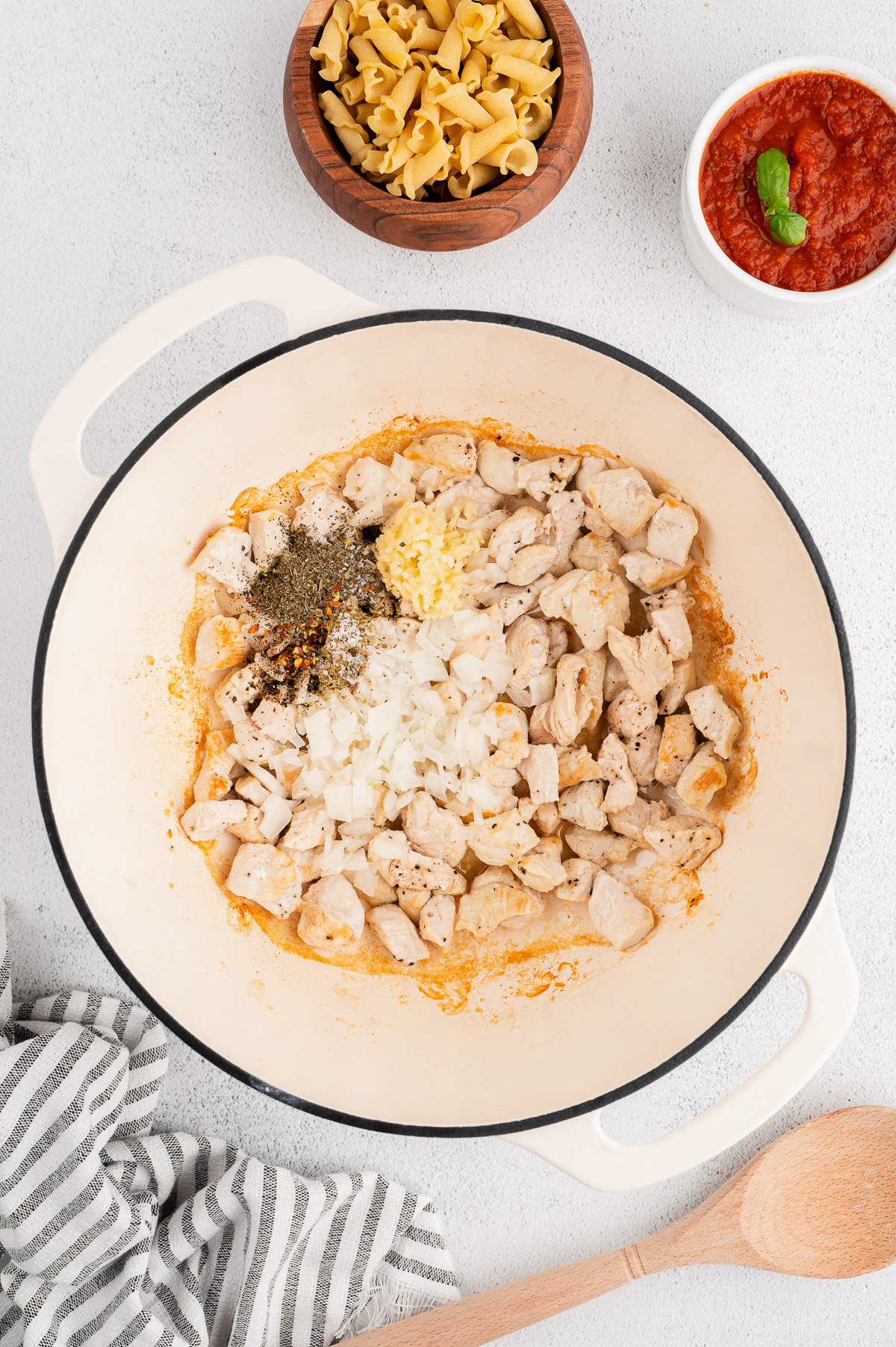 An overhead shot of a dutch oven with browned chicken and herbs for chicken parm pasta