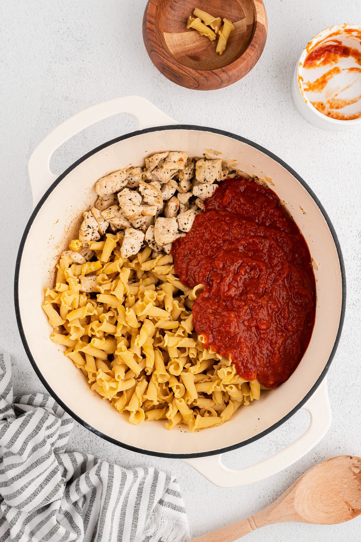 An overhead shot of a dutch oven with pasta, marinara sauce, and browned chicken for chicken parmesan pasta