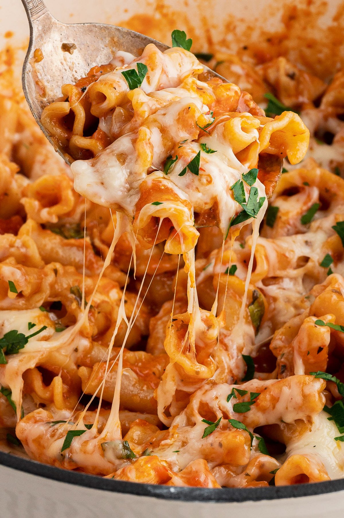 A spoon taking a large spoonful out of a pot of chicken parmesan pasta with an impressive cheese pull