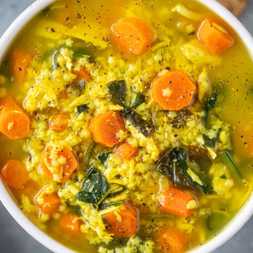 Chicken pastina soup in a white bowl on a grey counter with crackers on the side