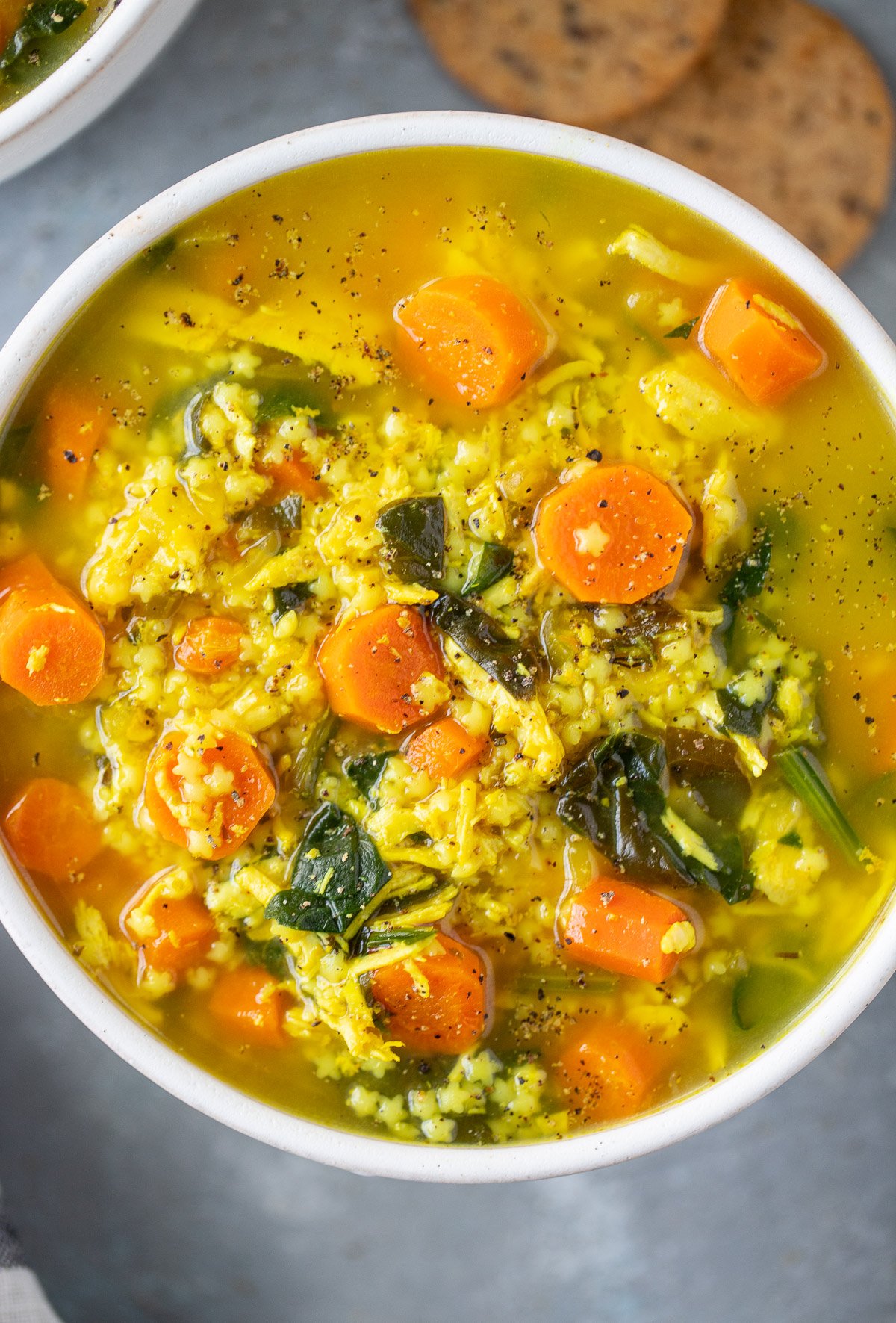 Chicken pastina soup in a white bowl on a grey counter with crackers on the side